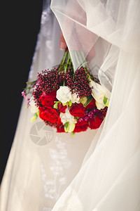 新娘握着红色和白玫瑰的婚礼花束图片