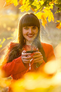在秋天公园喝热茶的笑女人近贴肖像图片