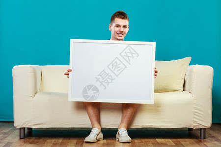 广告概念年轻人坐在沙发上用空白的演示文稿板男模型显示横幅标志广告牌复制蓝色文本的空间图片