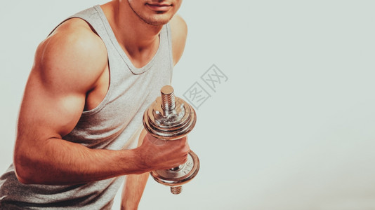健壮体的人与哑铃一起锻炼运动近身肌肉的年轻人举起灰色背角的重量图片
