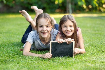 两个快乐的女孩肖像躺在草地上带着黑板图片