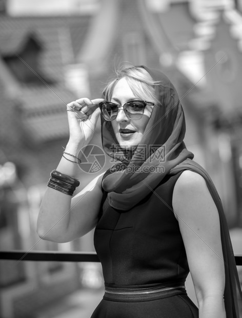 身着围巾和眼镜在街上摆姿势的优雅女子黑白近身肖像图片