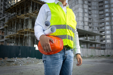 卡通手建筑师身穿黄色安全外套在建筑工地佩戴红色头盔背景