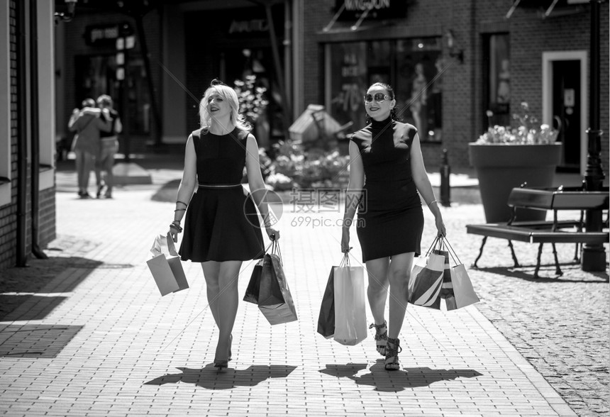 两名优雅妇女带着购物袋在街上行走的黑白照片图片