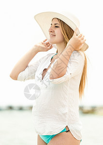 穿着帽子站在沙滩上看着地平线的优雅女人肖像图片