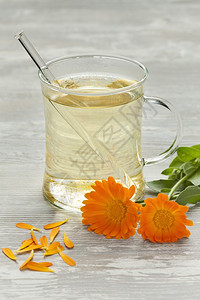 金盏花茶玻璃杯加茶壶马龙鲜花和叶子背景