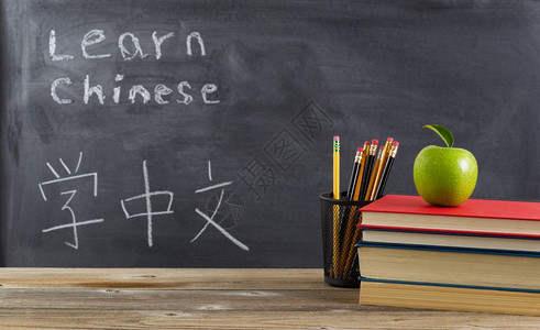 为学生习中文在纸板前用书本铅笔绿苹果和普通话文字背景图片