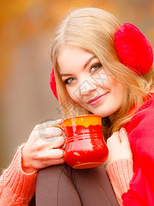 快乐的年轻女子在秋天公园享受热饮喝着红杯热饮橙叶背景图片