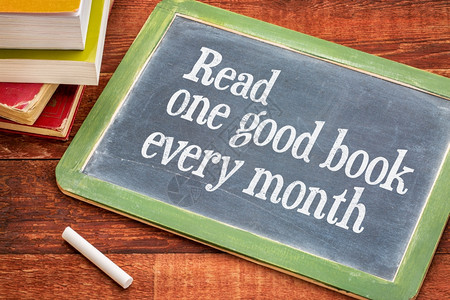 每月读一本好书在黑板上提供建议或醒用白粉和一堆书籍用铁制木餐桌对着铁的木餐桌图片