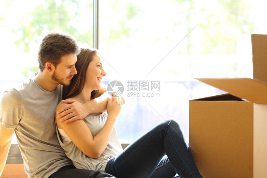 快乐的一对拥抱情侣着搬动新房子坐在地板上