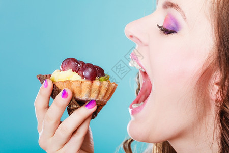 甜美的食物饱和脂肪的概念妇女面对张开的嘴吃蛋糕蓝背景图片