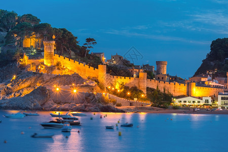 西班牙加泰罗尼亚州科斯塔布拉瓦岛托萨德马尔的堡垒和渔船夜景图片