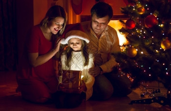 快乐的父母和可爱女儿看着圣诞礼物里面的图片