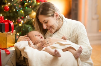 圣诞树下新生婴儿的幸福母亲肖像图片