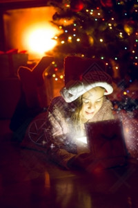 坐在圣诞树下看着闪发光的礼物盒可爱女孩肖像图片