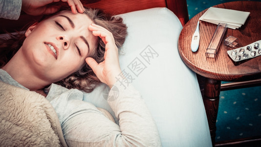 生病的妇女头痛躺在床上的女孩感冒温度计和药丸放在桌上图片