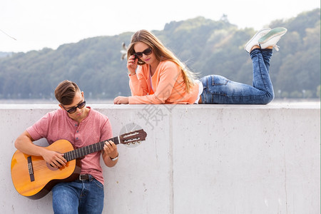 吉他主义者和的穆斯爱浪漫音乐天才激情约会概念吉他主义者和的缪斯年轻男子与躺在墙上有风景背的女孩一起弹吉他图片