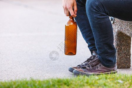 一个人在户外的长椅上被酒瓶压抑。 一个人在户外的长凳上被酒瓶压抑。 人们和酗酒问题。图片