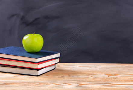 回到学校的概念绿色苹果和书在桌上的被抹掉黑板前图片