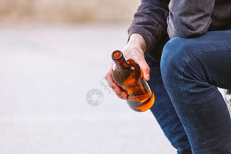一个人在户外的长椅上被酒瓶压抑。 一个人在户外的长凳上被酒瓶压抑。 人们和酗酒问题。背景图片