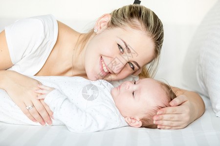 微笑的母亲与3个月大的婴儿躺在床上近镜像图片