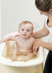 年轻母亲在洗手间帮她可爱的婴儿洗澡图片
