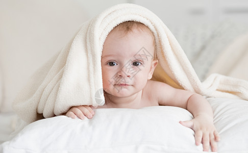 洗澡后躺在毛巾下床上的可爱小男孩肖像图片