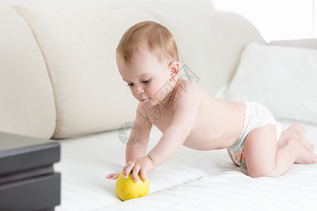 可爱的婴儿男孩爬在床上伸手拿苹果图片