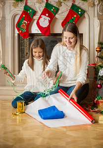 快乐的女儿和母亲在圣诞节前夕把毛衣包装在纸上背景图片