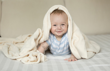 躺在白毯下床上的微笑男孩可爱肖像图片
