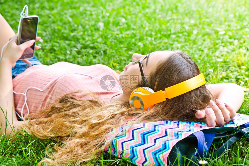 美丽的女孩在公园耳机里放松听音乐