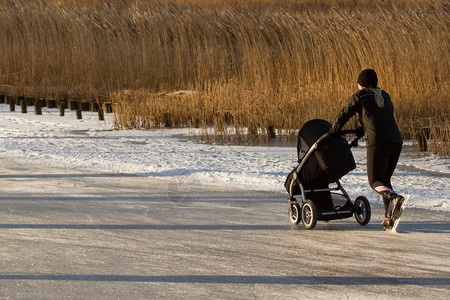 年轻母亲穿着冰刀鞋推着婴儿车在冰面上图片