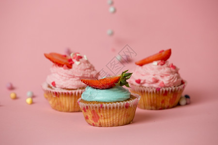 3个彩色纸杯蛋糕和草莓粉红色背景彩糖果的特拍镜头图片