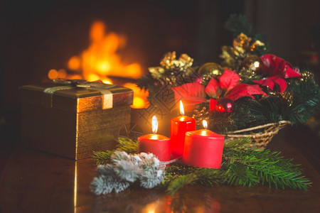 在起居室壁炉旁边的桌子上有燃烧蜡烛圣诞花圈和黄金礼品盒的紧贴图像图片