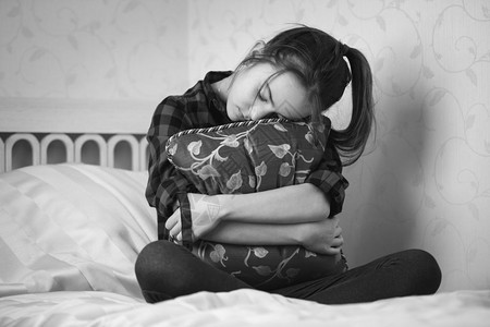 压抑的少女坐在床上抱着垫的黑白画面图片