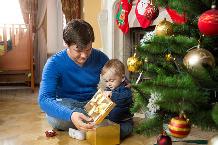 年轻父亲和可爱的小儿子在地板上打开圣诞礼物图片