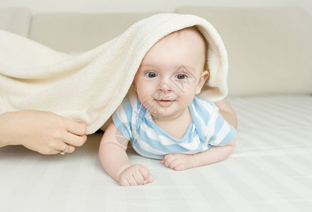 笑可爱的6个月婴儿男孩躺在床毛毯下上图片
