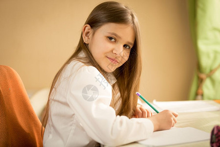 穿着白衬衫坐在桌后做功课的笑着黑头发女孩肖像图片