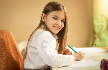 坐在办公桌后做功课穿着白衬衫的笑女孩肖像图片
