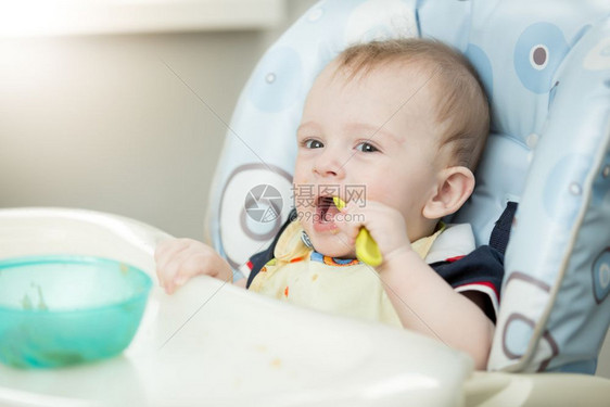 可爱的婴儿男孩在厨房用高椅子勺吃饭图片
