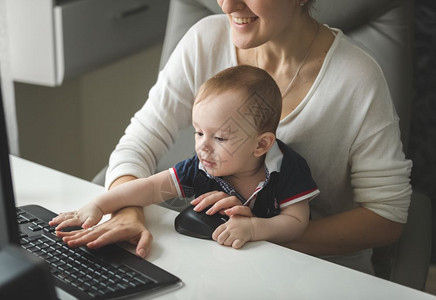 微笑的女商人在电脑上工作婴儿男孩坐在她的腿上图片