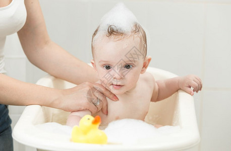 婴儿男孩用黄色橡胶鸭在泡沫浴中玩图片