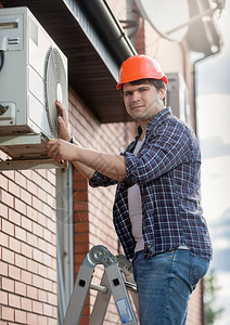 在建筑外墙上安装空调机的年轻工程师技术员高清图片素材