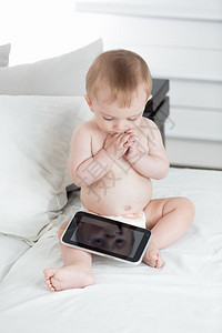 坐在床上和数字平板电脑上玩耍的尿布中可爱婴儿图片