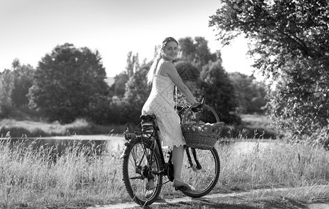 美丽女子骑着自行车在河边的黑白照片图片