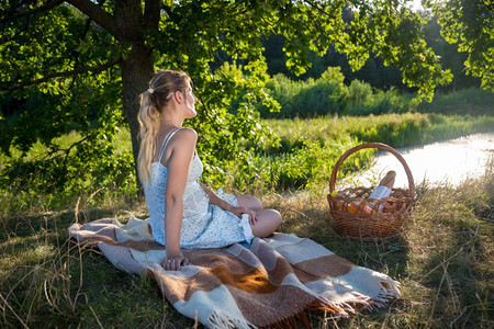 户外野餐坐在田地大树下看着湖的年轻女子背景