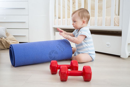 可爱的婴儿男孩玩哑铃和健身垫图片