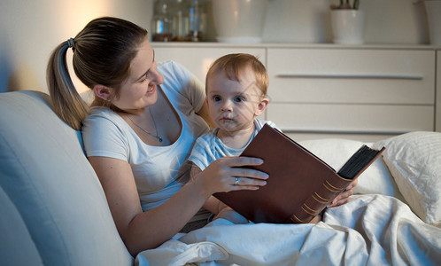 年轻母亲晚上和婴儿躺在床拿着大本书图片