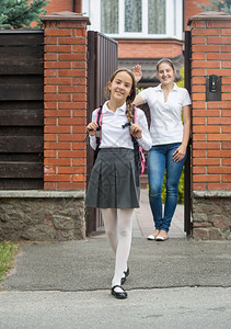 微笑的女孩走出家门上学母亲站在门口向她挥手情绪高清图片素材