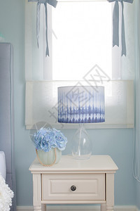 在浅蓝色室内卧床边桌的鲜花罐和阅读灯图片